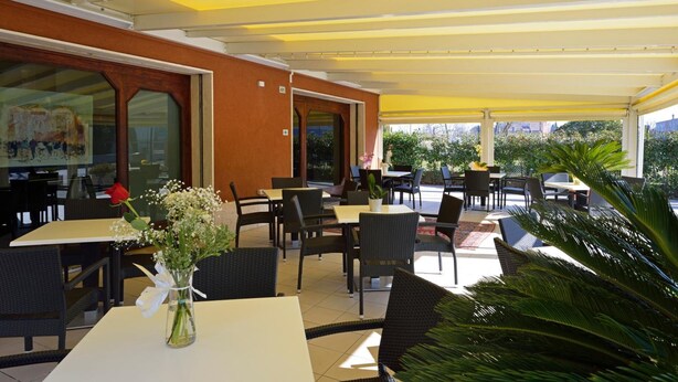 An outdoor cafe with tables and chairs, a yellow awning, and a view of the city. - Albergo Italia (Porto Tolle)