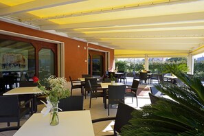 An outdoor cafe with tables and chairs, a yellow awning, and a view of the city. - Albergo Italia (Porto Tolle)