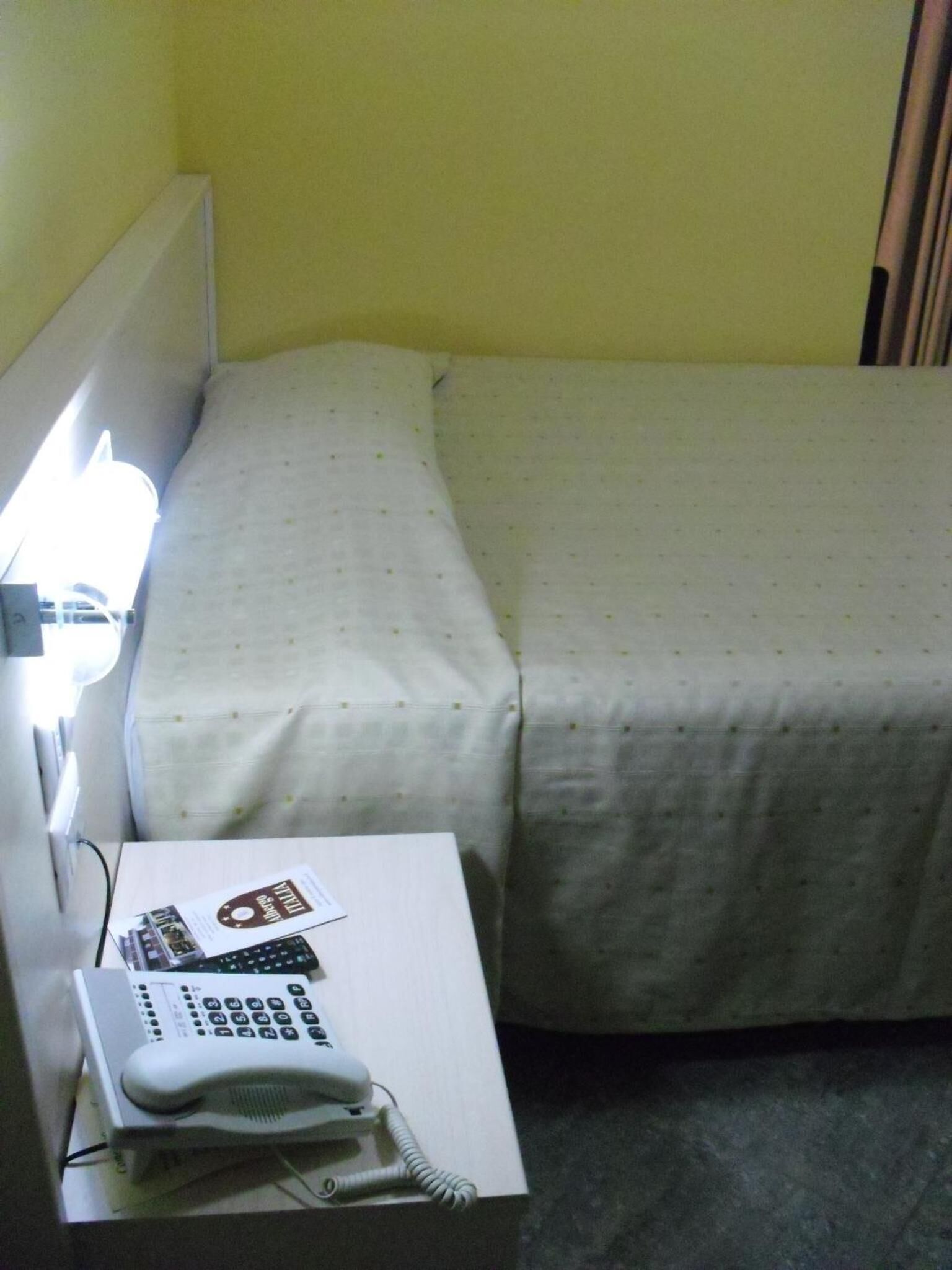 Quarto de hotel com cama, mesa de cabeceira e luminária.