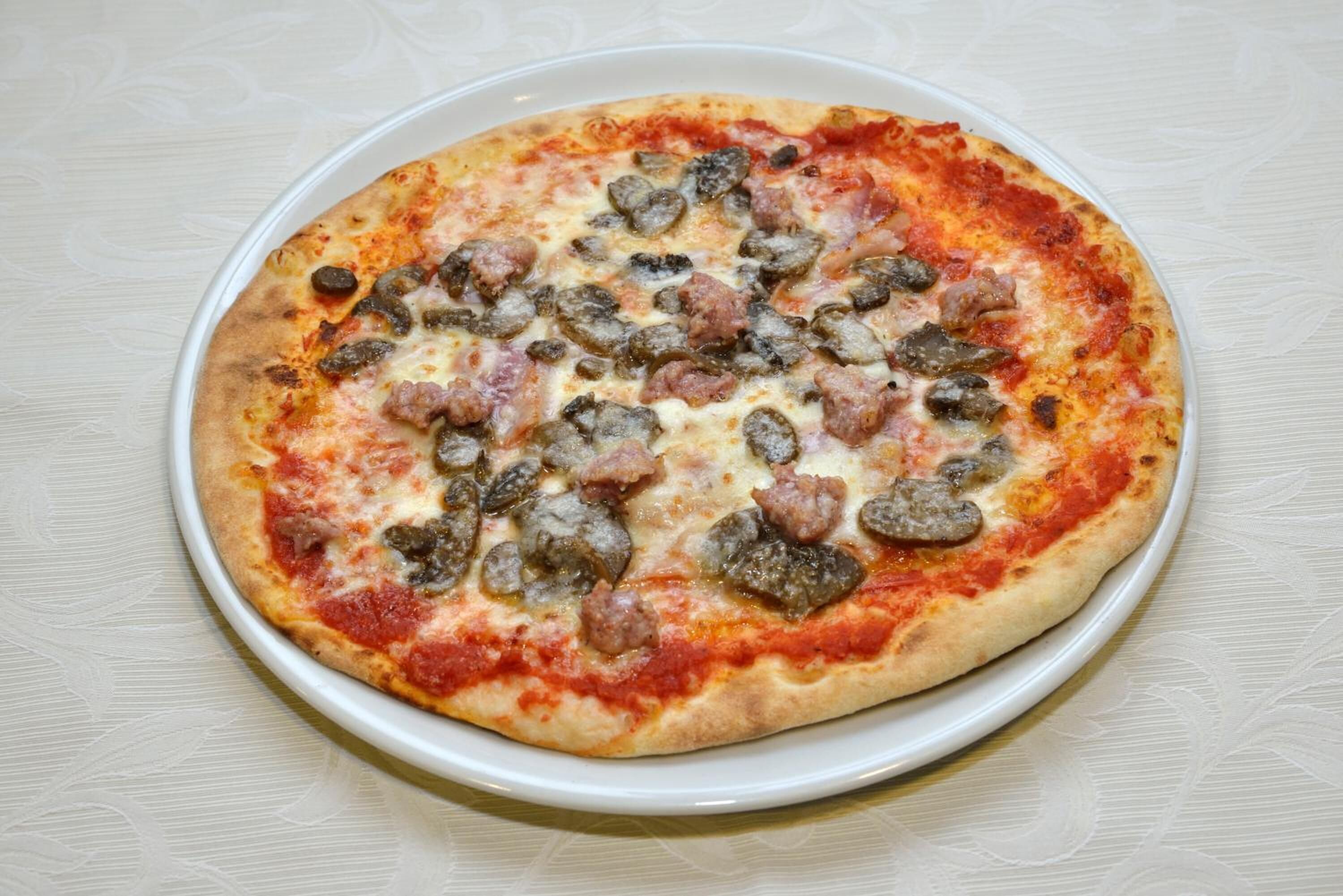 Una pizza con salchicha y champiñones sobre un plato blanco.