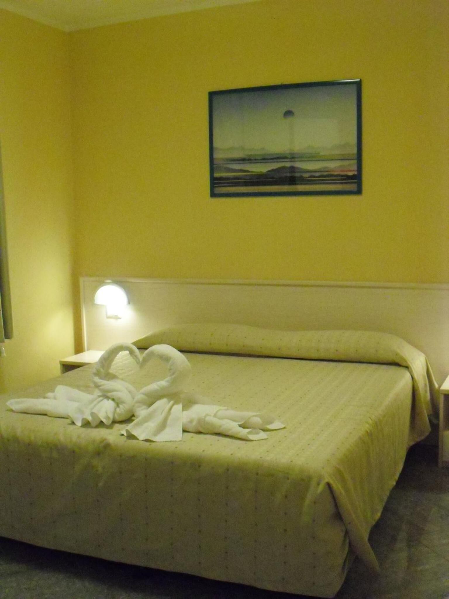 Una habitación de hotel con una cama, una mesita de noche, una lámpara y un cuadro en la pared.