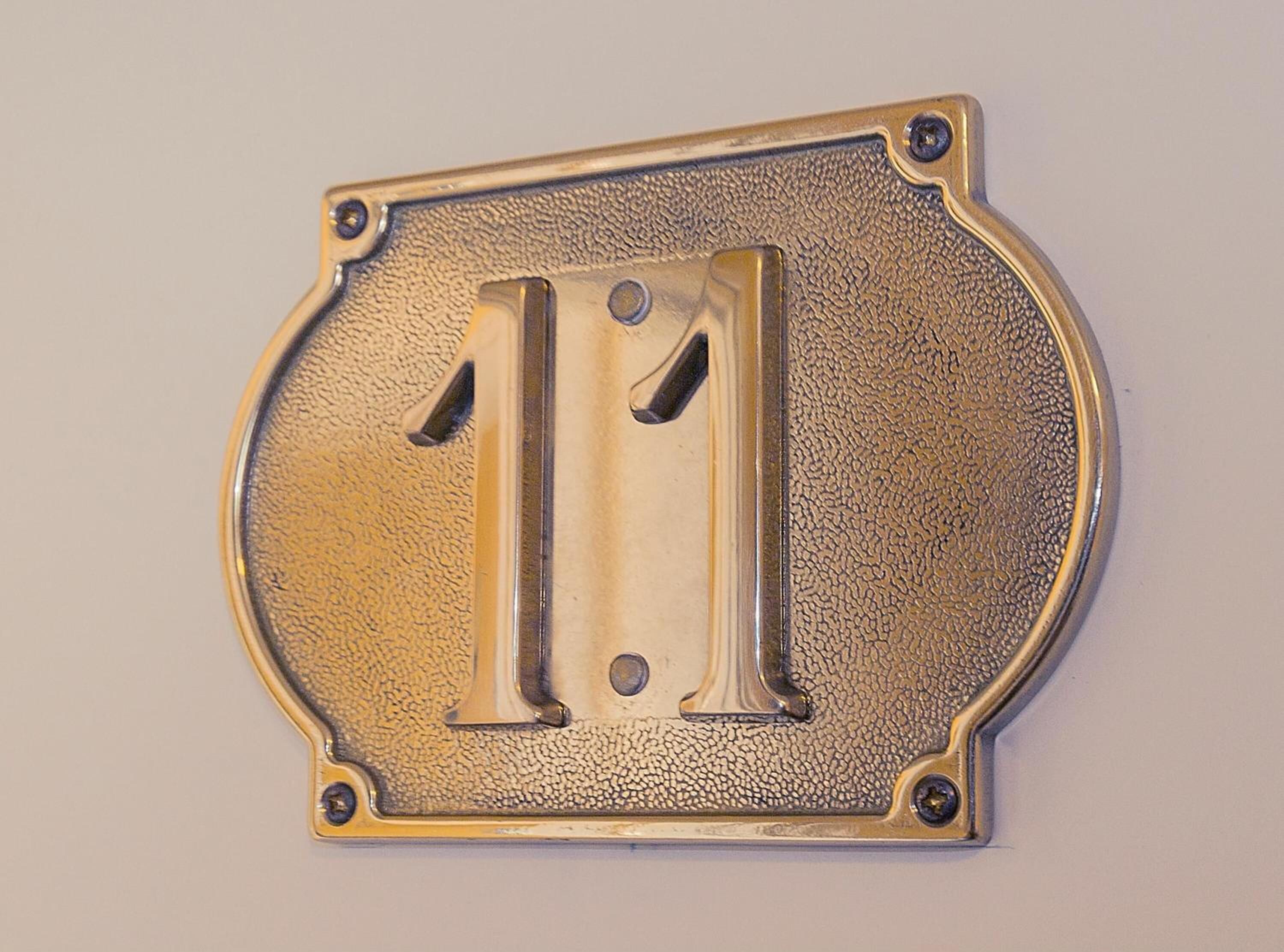 A metallic number plaque with the number 11, mounted on a textured surface.