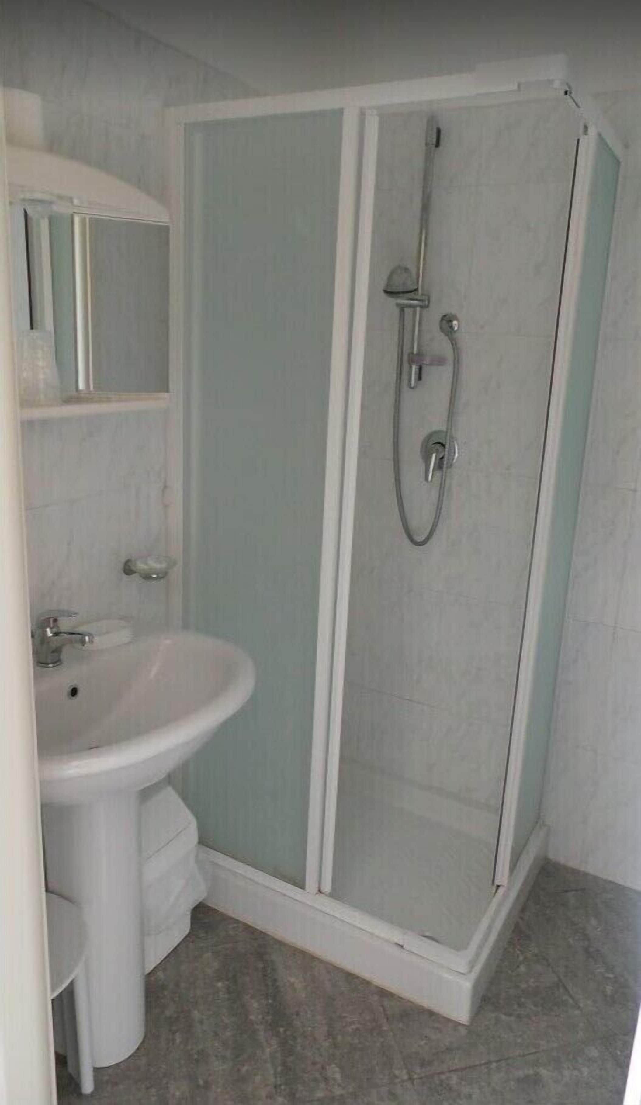 Ein Badezimmer mit einer gläsernen Duschkabine, einem Standwaschbecken und einem Spiegel darüber.