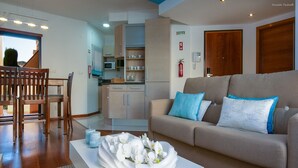A modern living room with a sofa, a dining table with chairs, a kitchen area, and a view of the outside. - A24 - LuzBay Beach Apartment by Dreamalgarve (Lagos)