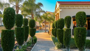 A pathway lined with neatly trimmed topiary trees leading to a pool area with lounge chairs. - A24 - LuzBay Beach Apartment by Dreamalgarve (Lagos)
