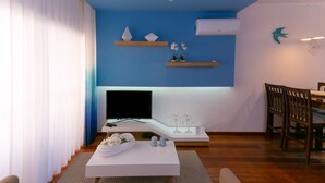 A modern living room with a flat-screen TV, a white coffee table, and a dining area with wooden chairs. - A24 - LuzBay Beach Apartment by Dreamalgarve (Lagos)