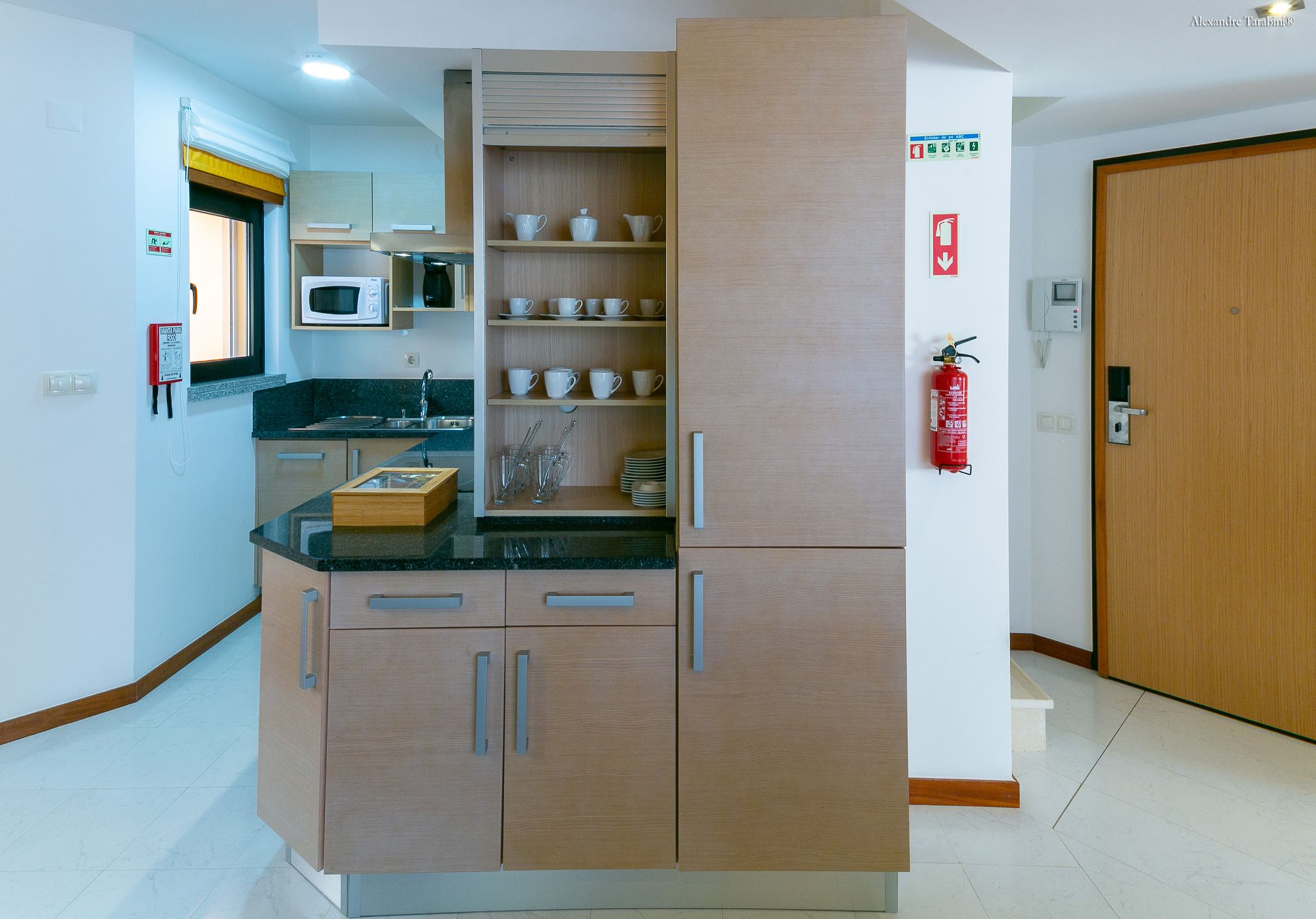 A compact kitchen with a microwave, a sink, and a cabinet with shelves for dishes.