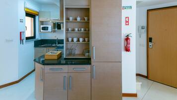 A compact kitchen with a microwave, a sink, and a cabinet with shelves for dishes.