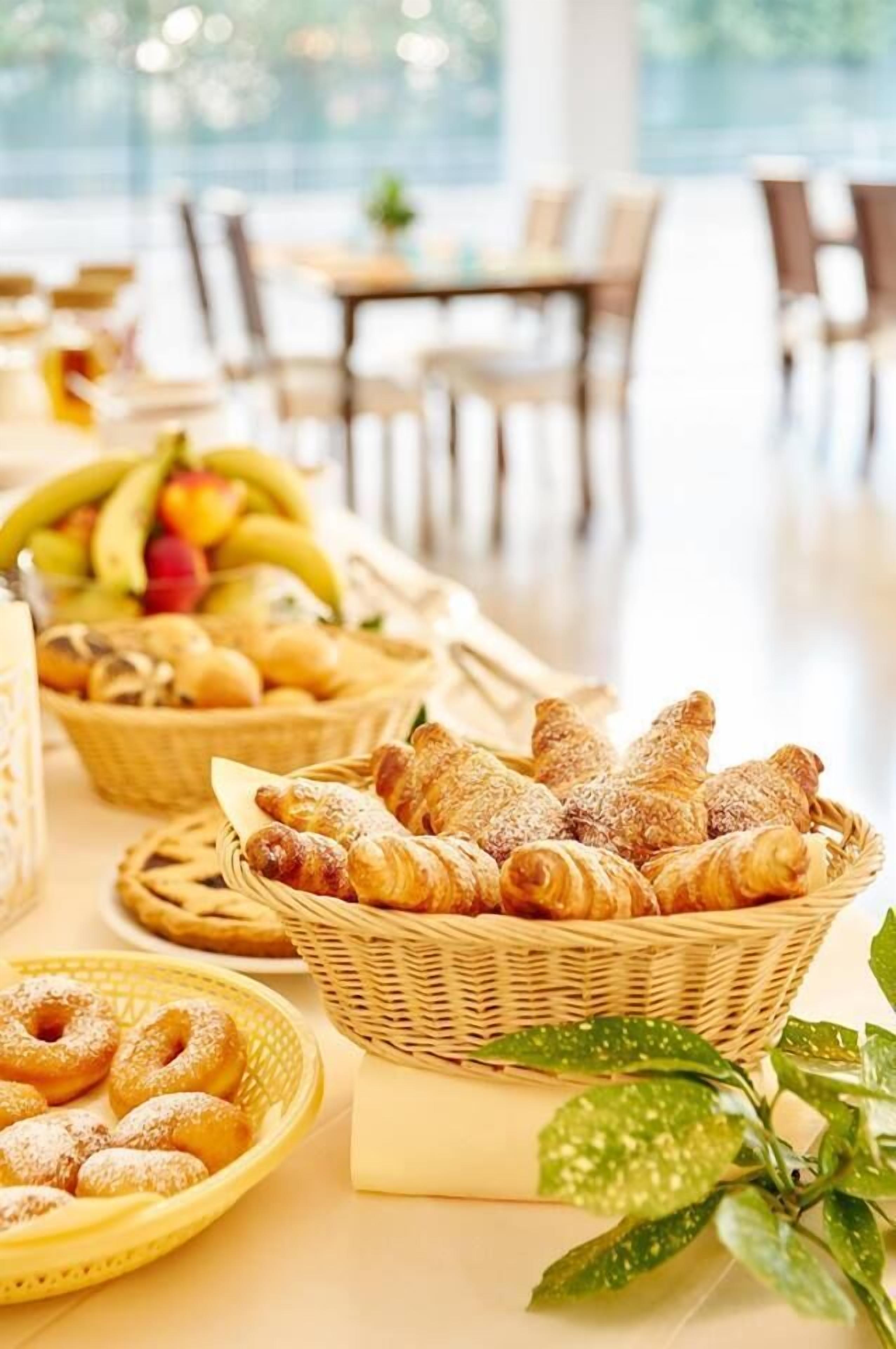 A buffet table with various baked goods, including pastries and donuts, and a fruit basket in the background.