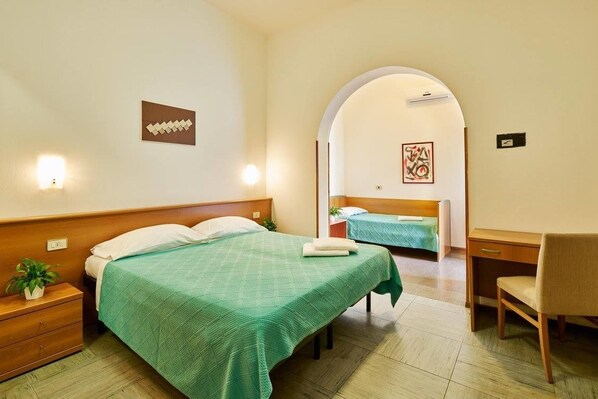 A hotel room with two beds, a desk, a chair, and a small plant.