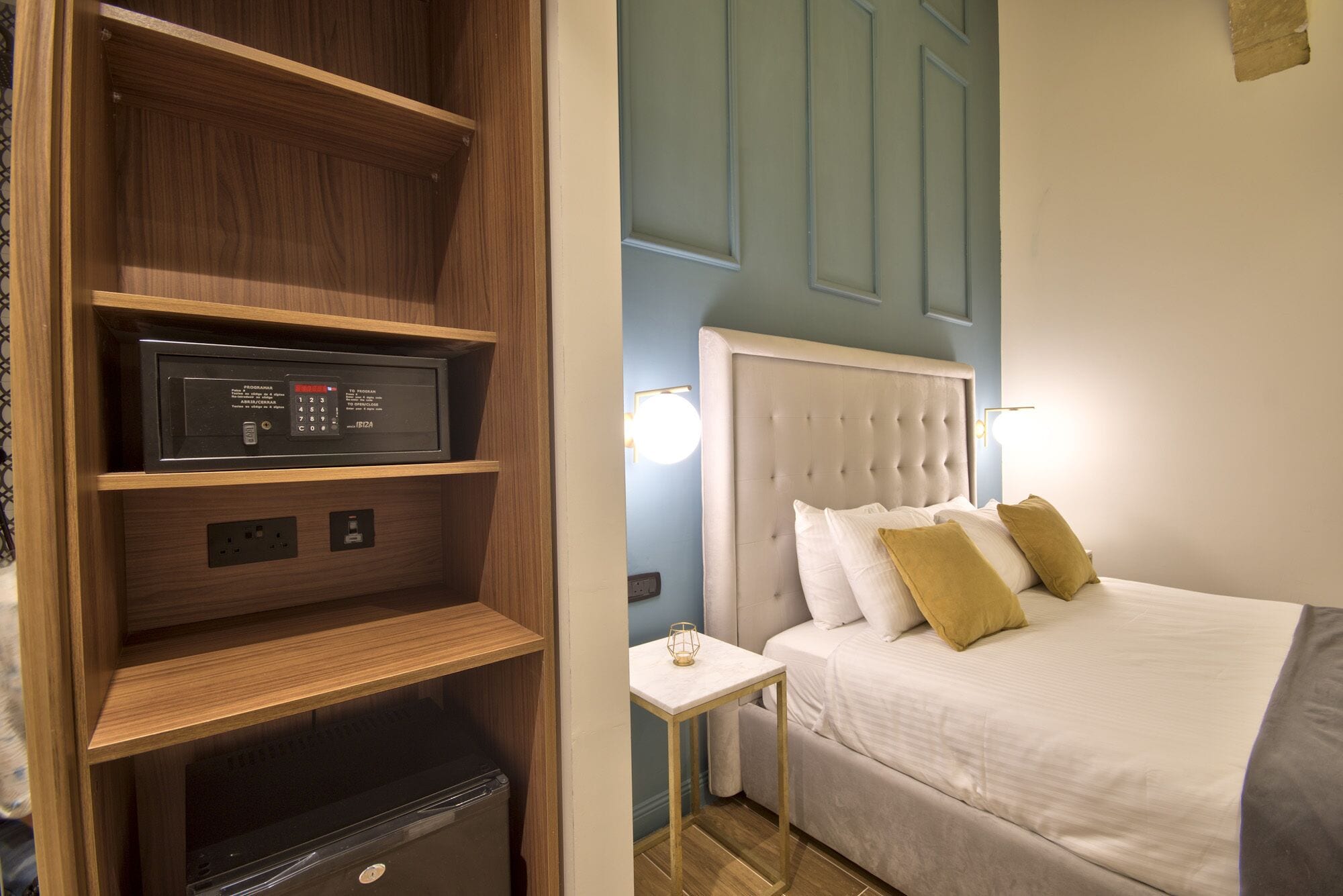 Una habitación de hotel con cama, mesita de noche, televisor integrado y minibar.