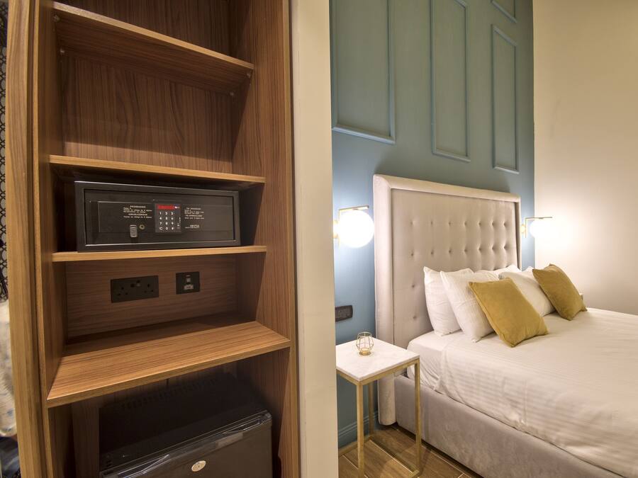 Una habitación de hotel con cama, mesita de noche, televisor integrado y minibar.
