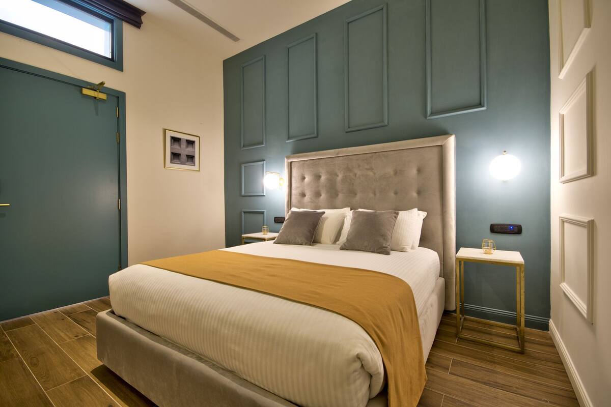 A bedroom with a large bed, a bedside table, a nightstand, a window, and a door.