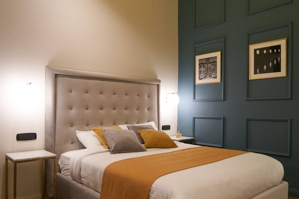 A bedroom with a large bed, wooden flooring, a blue accent wall, and framed pictures.