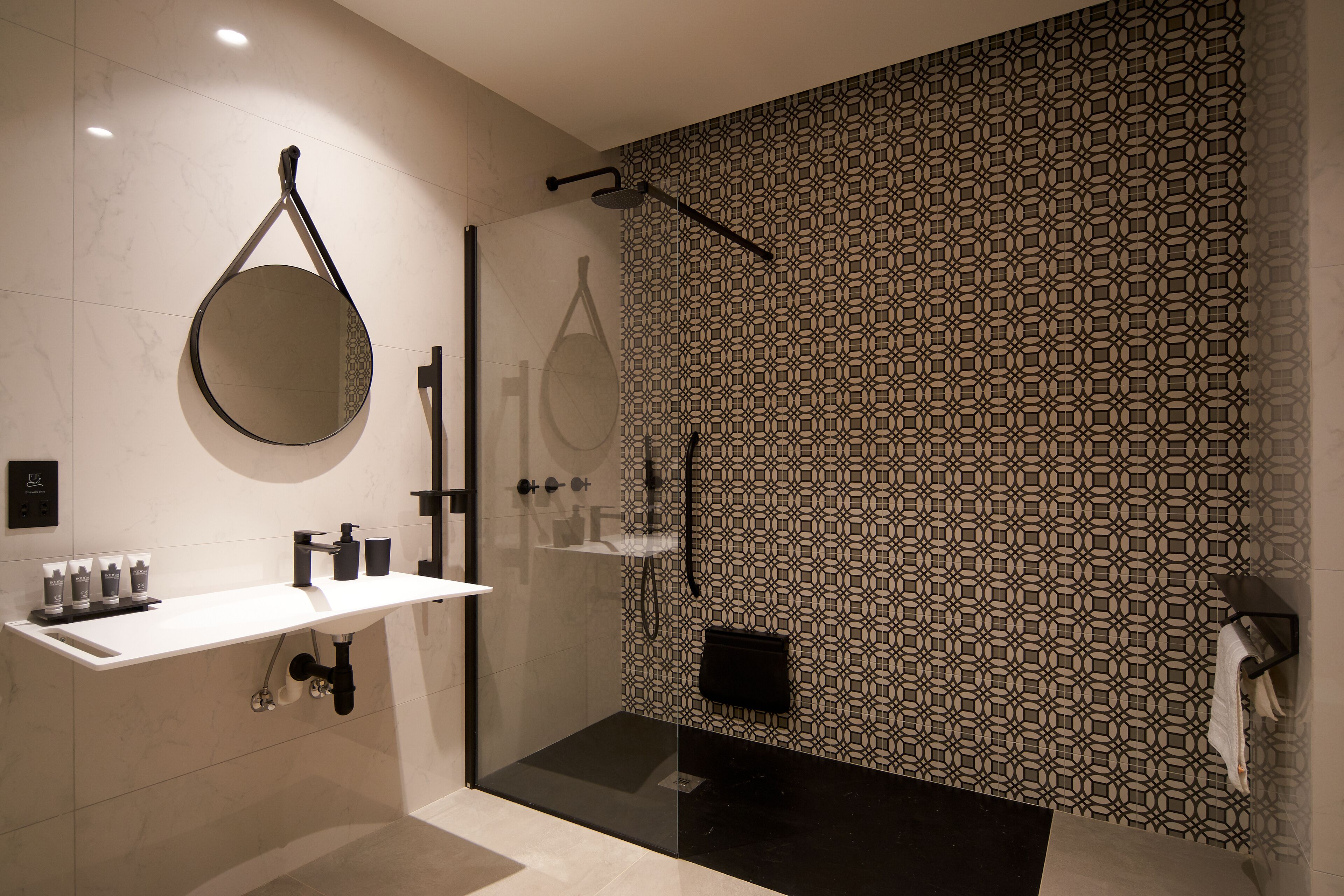 A modern bathroom with a glass shower enclosure, a white vanity with toiletries, and patterned wall tiles.