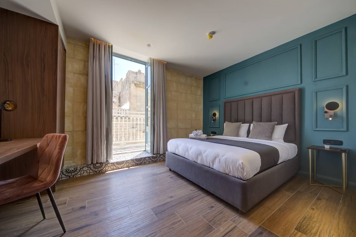 A modern hotel room with a large bed, a desk, and a view of the city.