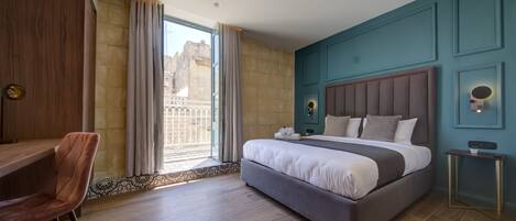 A modern hotel room with a large bed, a desk, and a view of the city.