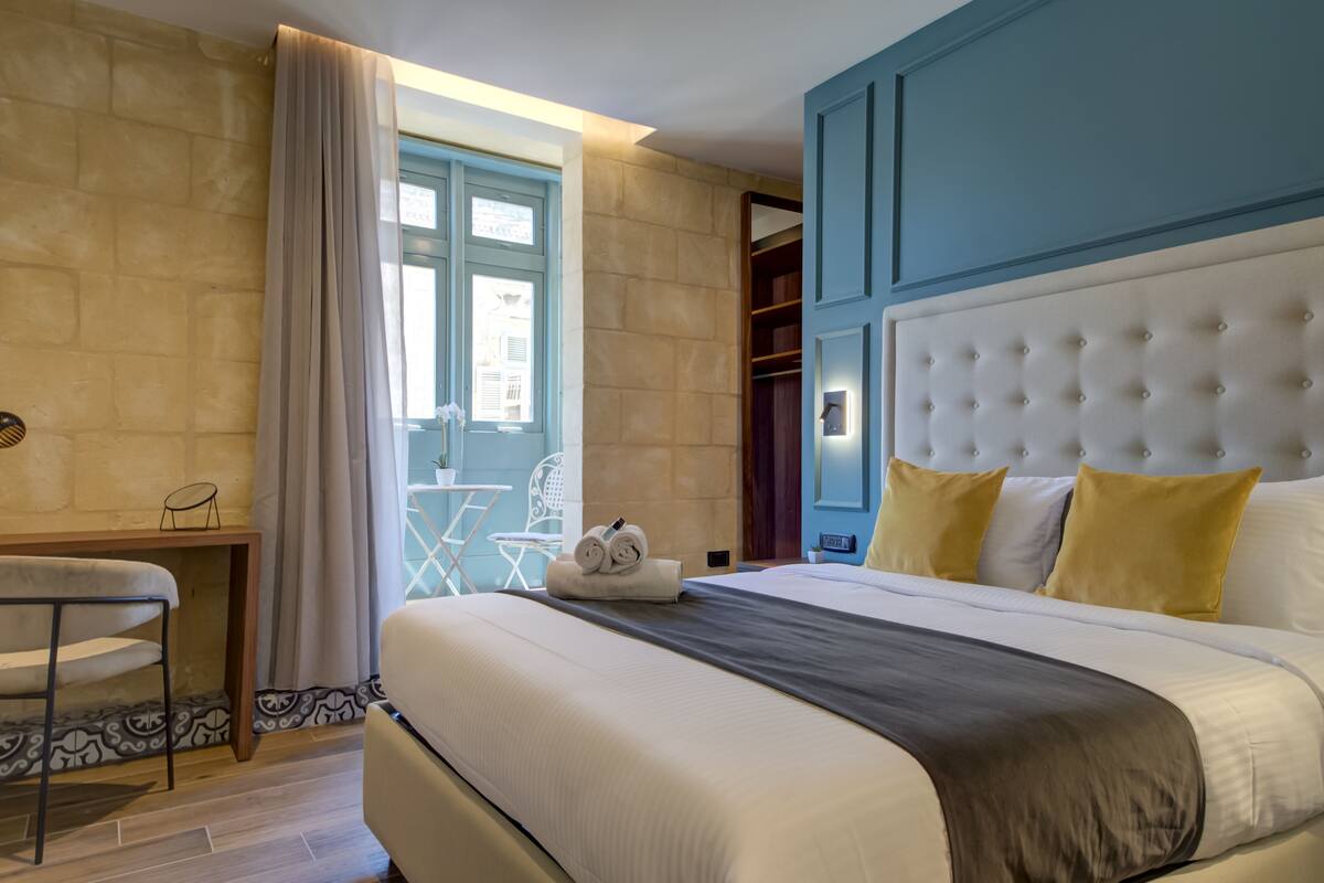 A hotel room with a large bed, a desk, a chair, and a window with curtains.