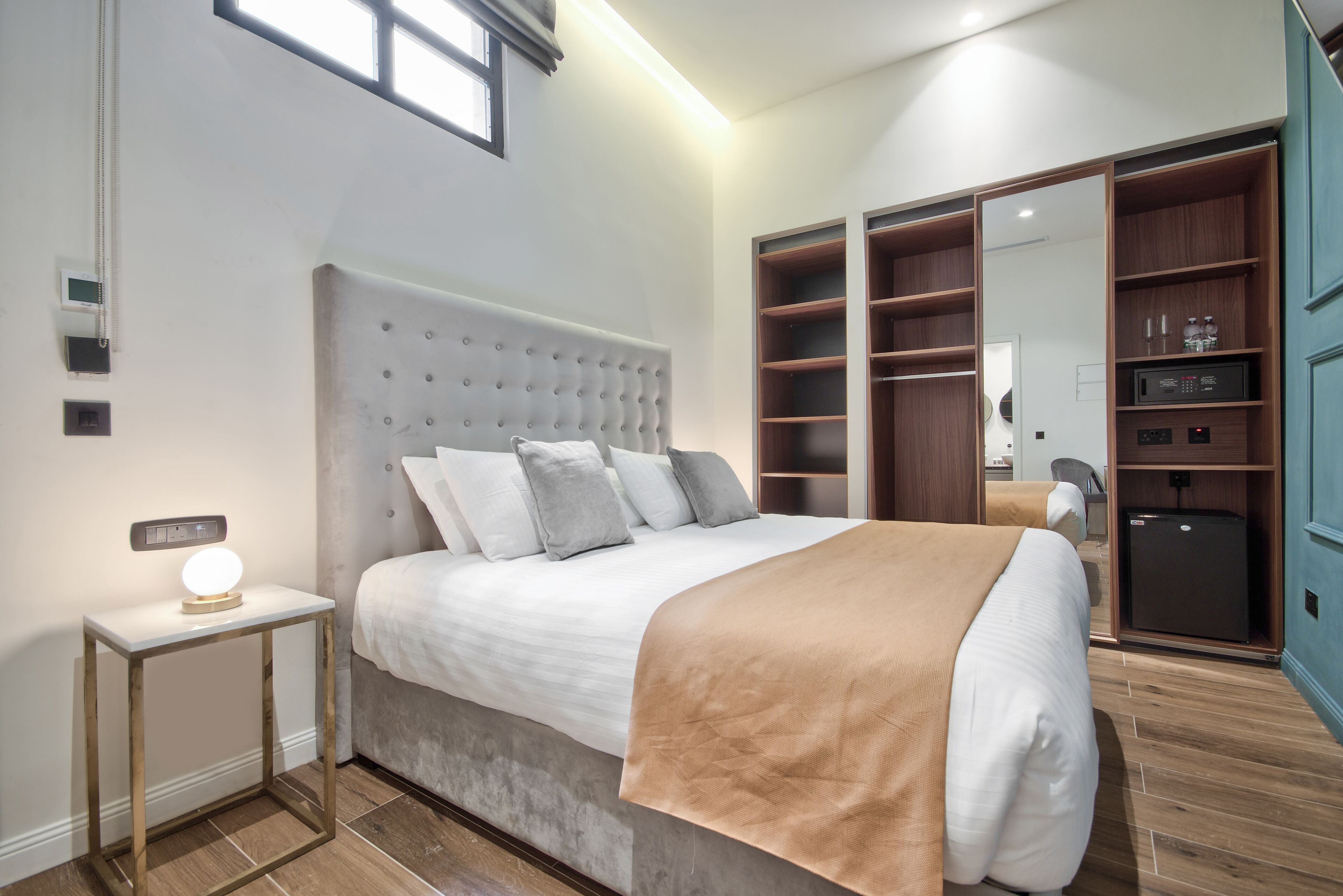 Un dormitorio con una cama grande, una mesita de noche con lámpara, un armario con estantes y un espejo.