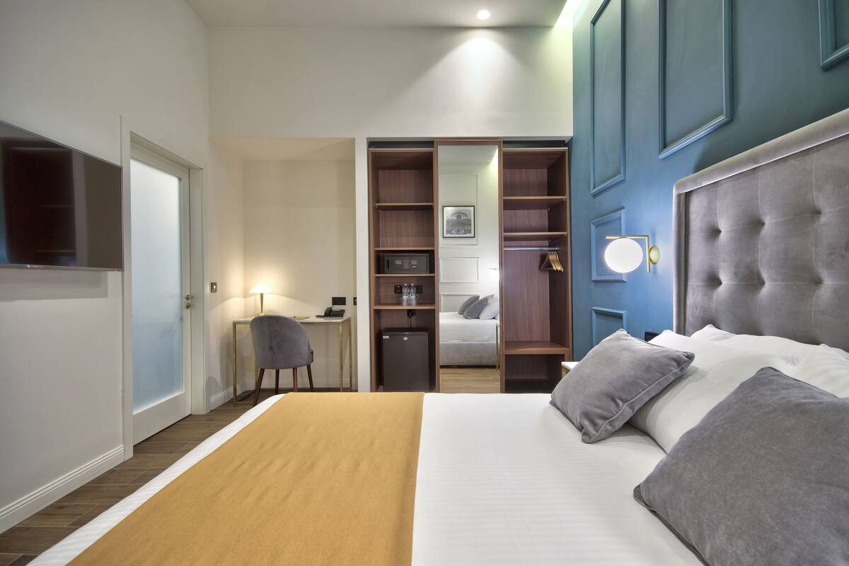 A hotel room with a bed, a desk, a chair, a wardrobe, and a mirror.
