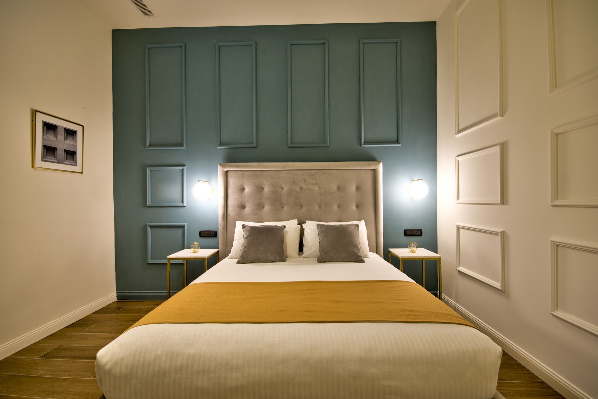 A bedroom with a large bed, two bedside tables, a headboard, and wall-mounted lighting.