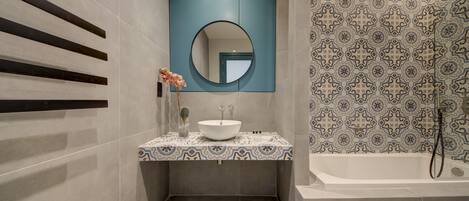 A modern bathroom with a large bathtub, a round mirror, and a patterned tile backsplash.