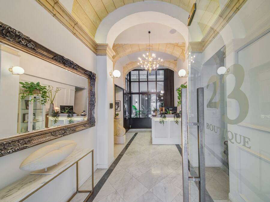 A hallway with a marble floor, a large ornate mirror, a reception desk, and a chandelier.