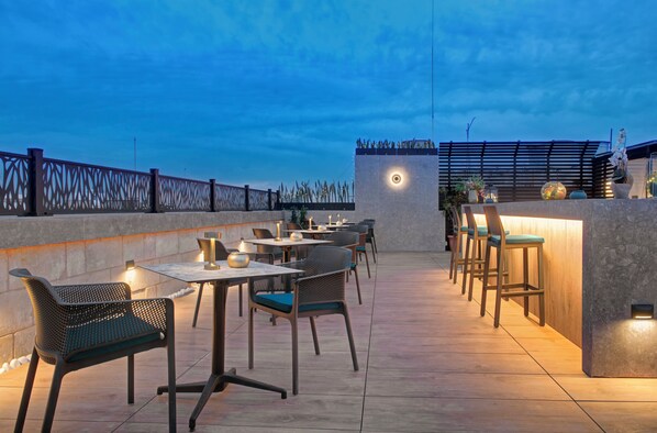 An outdoor dining area with tables and chairs, a bar, and a decorative wall with a light fixture. - 23 Boutique (Floriana)