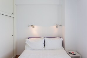 A bedroom with a bed, white walls, and a nightstand with a book. - Sea View Balcony, Steps from Beach and Old Town (Chania)