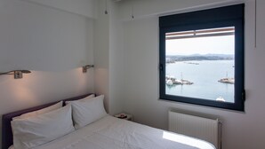 Ein Schlafzimmer mit einem Bett, einem Fenster mit Blick auf ein Gewässer und Booten, sowie einem Wandheizkörper.