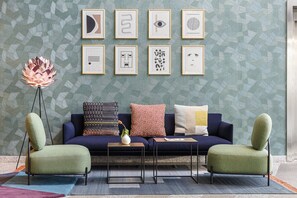 Un salon moderne comprenant un canapé, deux fauteuils, une lampe sur pied et une table basse. Des œuvres d’art encadrées ornent le mur.