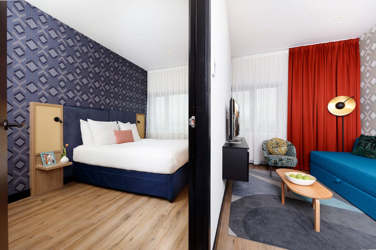 Une chambre d’hôtel avec un lit, un canapé, une télévision, une petite table avec un bol et une chaise.