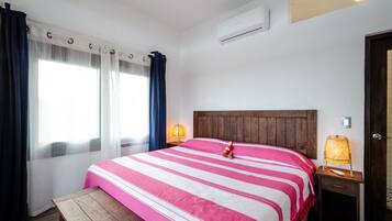 A hotel room with a bed, a nightstand, a lamp, and a window with curtains.