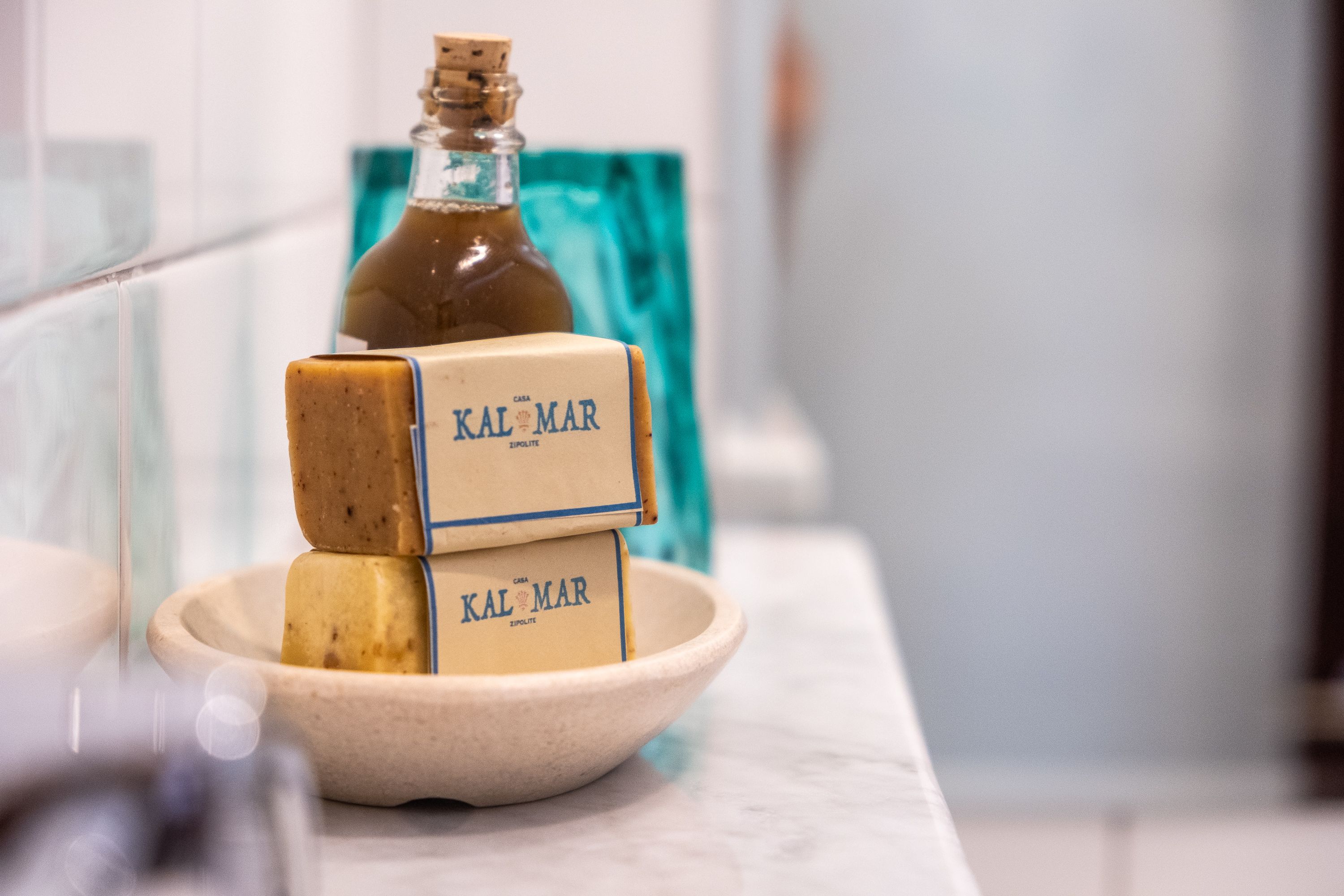 Een badkamer met een marmeren aanrechtblad, een glazen fles en twee zeepstaven met de aanduiding "KAL MAR".