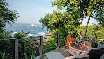 Un balcon avec vue sur l’océan, des chaises en bois et une table.