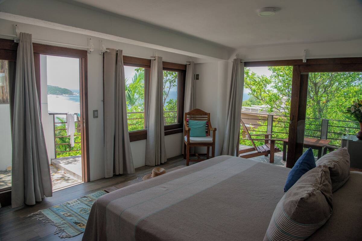 A bedroom with a large bed, a chair, and a view of the outdoors.