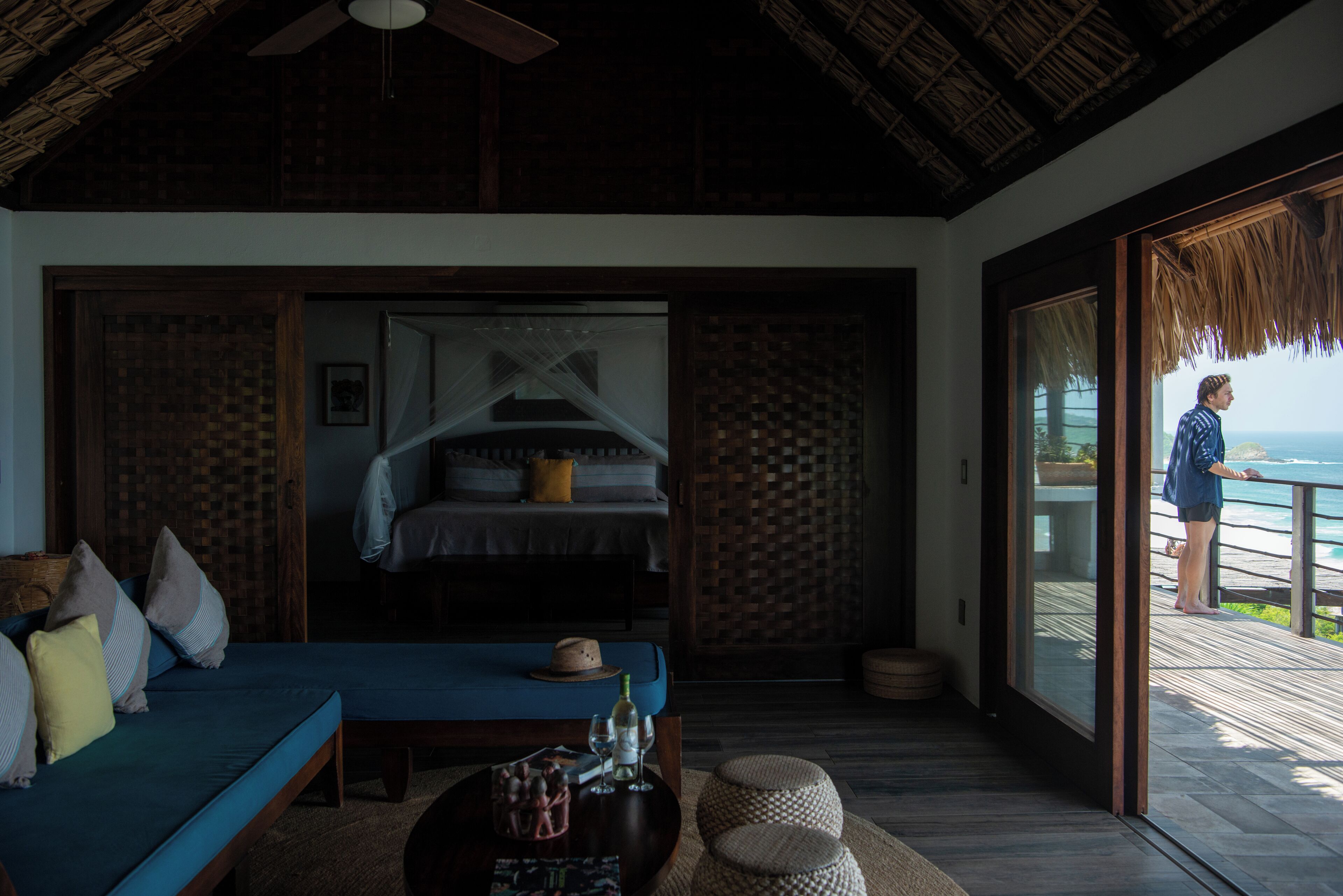 A bedroom with a bed, a sofa, a coffee table, and a balcony with a view of the ocean.
