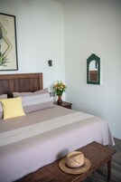 Un dormitorio ordenado con una cama, almohadas, una mesita de noche, un jarrón con flores y un espejo en la pared.
