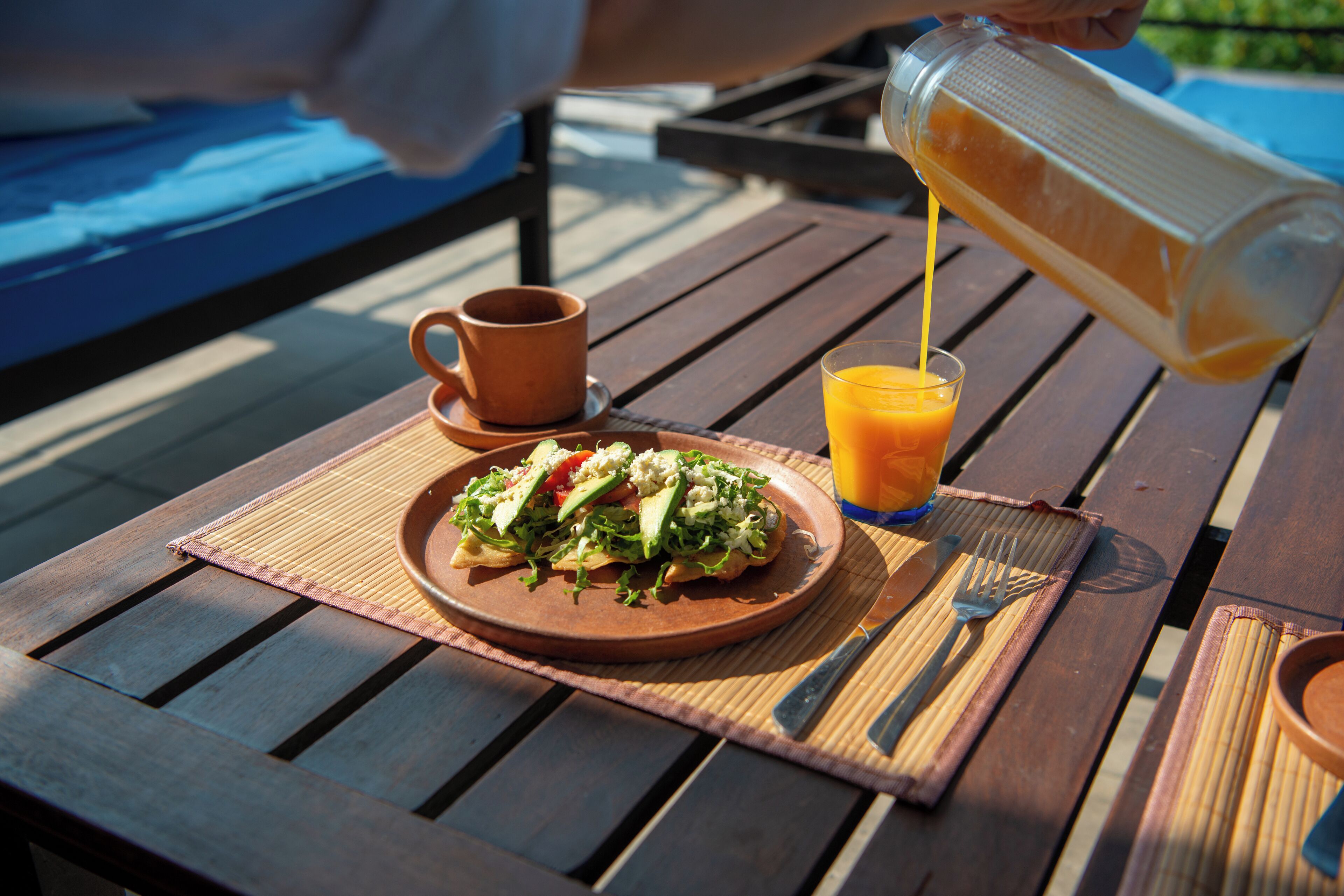 Une table en bois avec une assiette de nourriture, un verre de jus d’orange et une tasse.