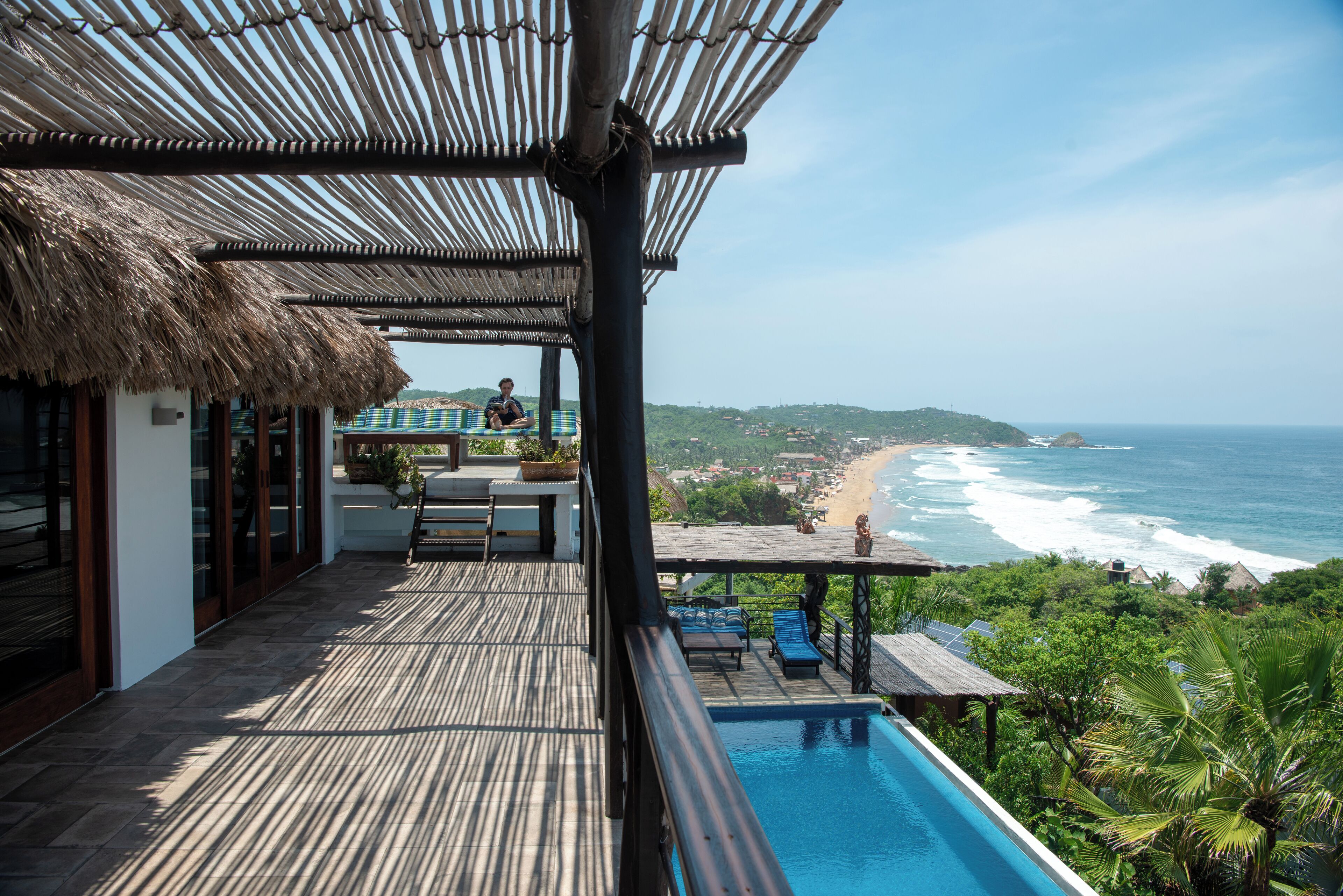 Terraza de madera con piscina, con vistas a una playa y al océano.