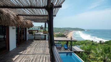 Terraza de madera con piscina, con vistas a una playa y al océano.