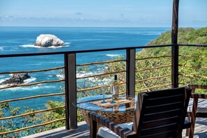 A table with a bottle and glasses, overlooking a coastal view with a rocky outcrop and greenery. - Casa KalMar (Santa María Tonameca)