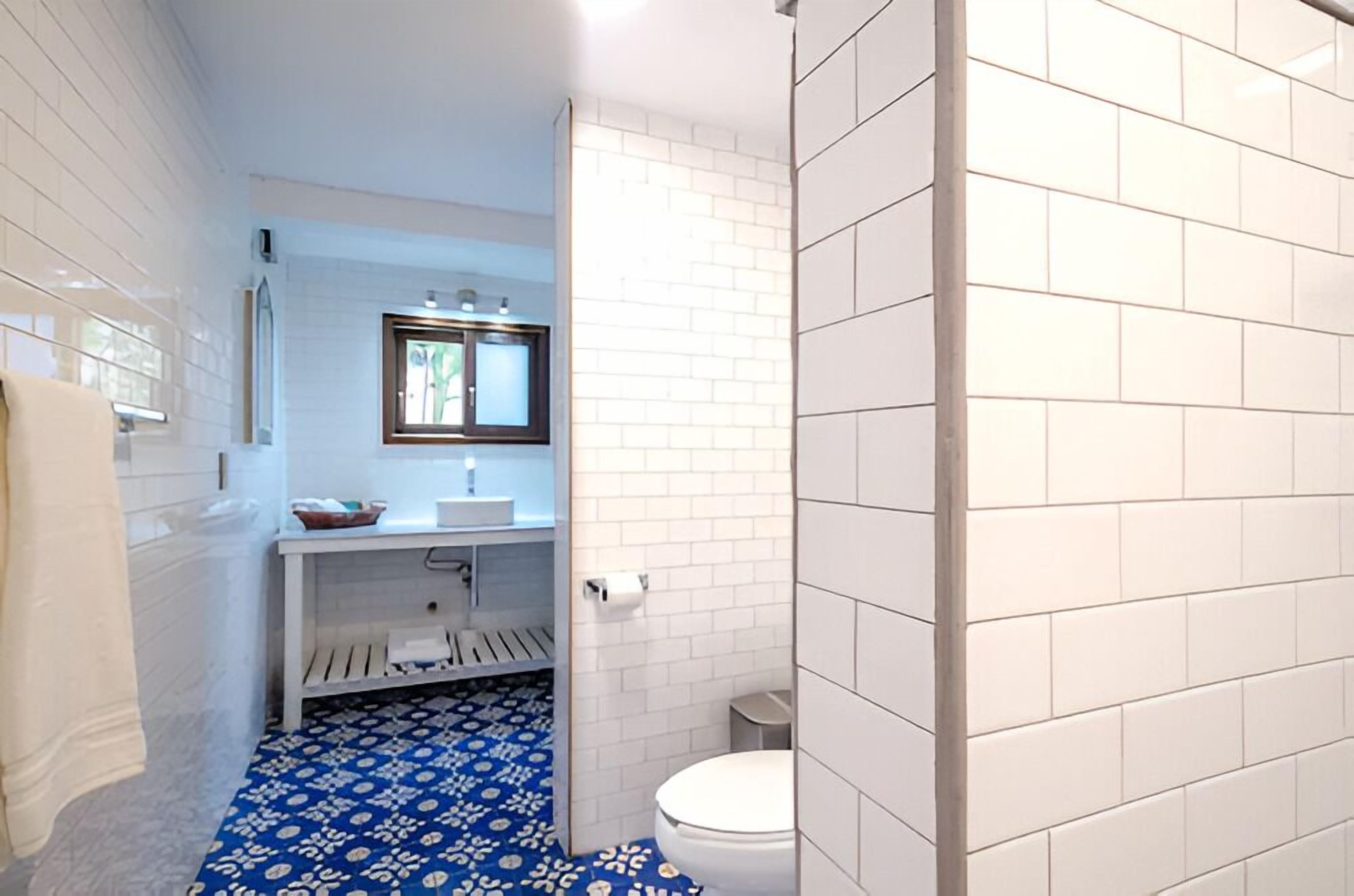 A bathroom with white tiled walls, a blue patterned floor, a white sink, and a toilet.