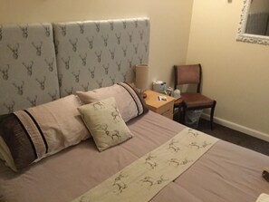 A hotel room with a large bed, a nightstand, a chair, and a mirror on the wall. - Harbour Bridge Camps Bar (Wick)