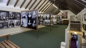 Una galeria d'art amb fotografies emmarcades exposades, bancs de fusta i un sostre alt amb bigues al descobert.