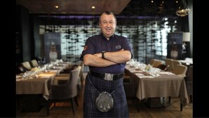 Un home amb kilt al bell mig d'un restaurant, amb taules preparades per dinar.