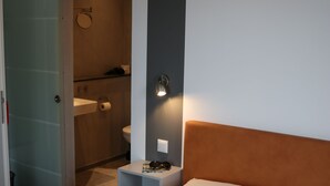 Habitación de hotel con cama, mesita de noche y baño visible a través de una puerta abierta.