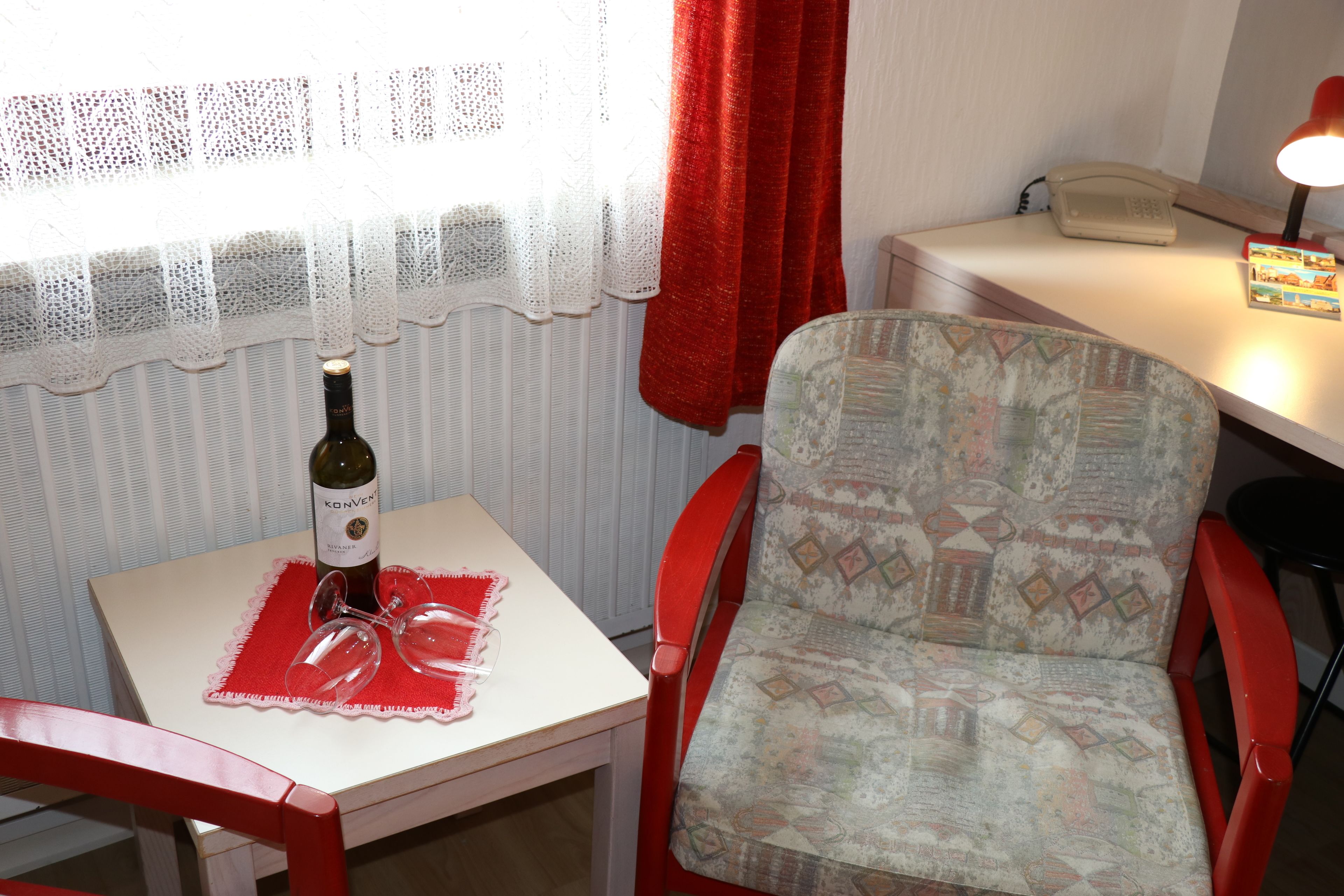 A small room with a table, a chair, a bottle of wine, and a telephone.
