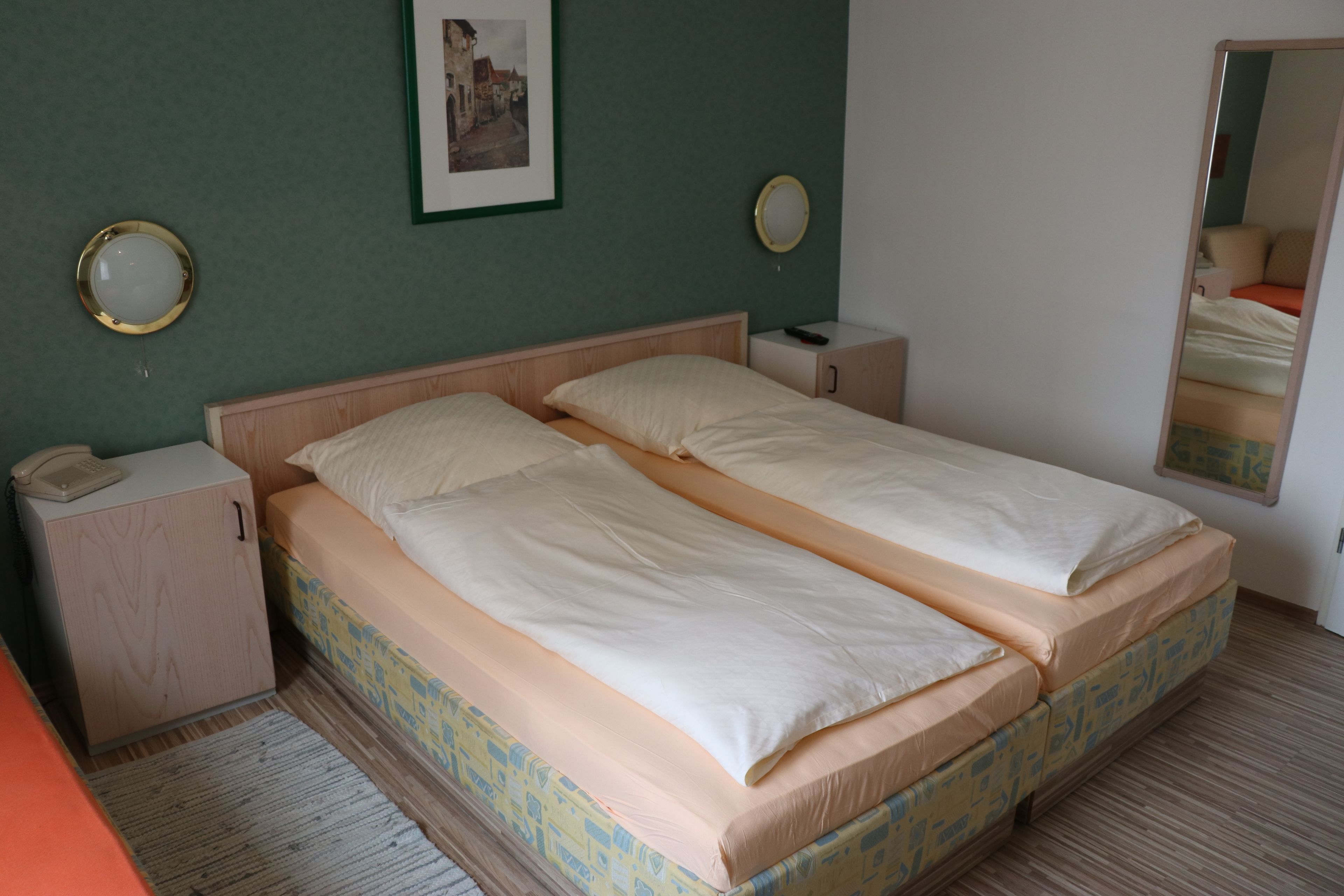 A double bed with a wooden headboard, a bedside table with a lamp, a small cabinet, and a framed picture on the wall.