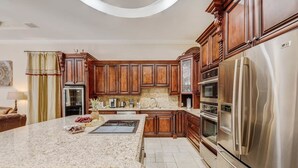 A kitchen with granite countertops, wooden cabinets, stainless steel appliances, and a central island with fruit. - VIP Accommodations (Hollywood)